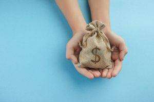 Women hold a money bag on light blue background, Saving money for future investment concept.