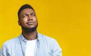 Portrait of suspicious black guy looking upwards at copy space on yellow background.