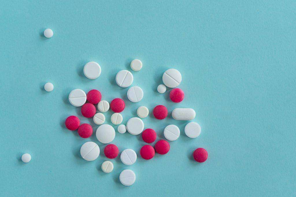White and red pills of various shapes scattered on a blue background. Top view.