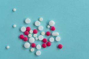 White and red pills of various shapes scattered on a blue background. Top view.